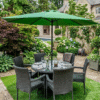Round 6-seater grey rattan dining set with a large green patio umbrella, set for brunch on a stone patio with lush garden greenery and white hydrangeas.
