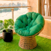 A luxe emerald green papasan swivel chair on a modern high-rise balcony with artificial turf, overlooking a golden city sunset.