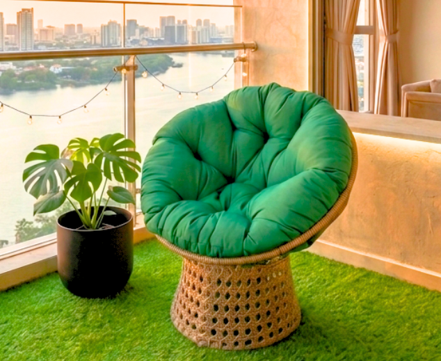 Screenshot 2026-03-23 134606 A luxe emerald green papasan swivel chair on a modern high-rise balcony with artificial turf, overlooking a golden city sunset.