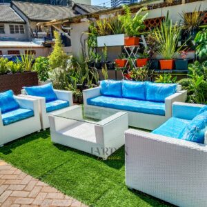 A large 7-seater white rattan sofa featuring a 3-seater sofa, two 2-seater loveseats, and a glass coffee table with blue cushions on turf grass.