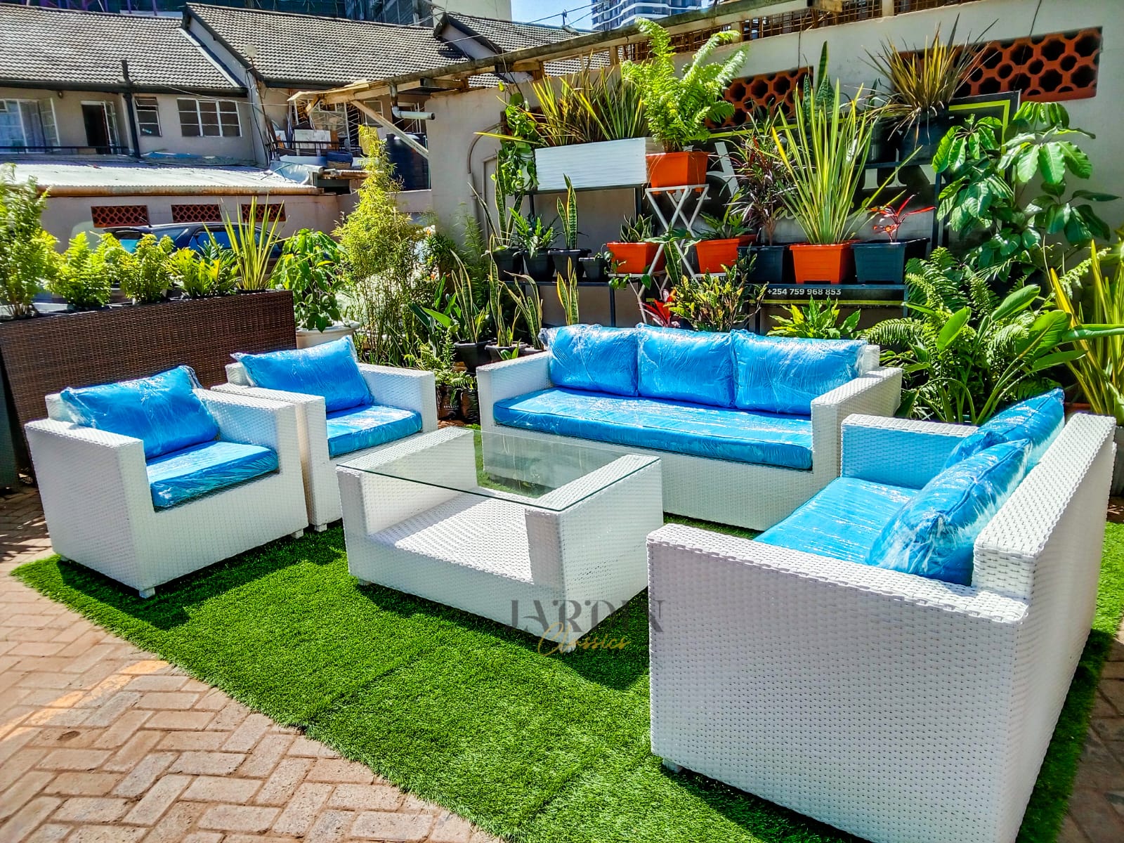 Jasmine A large 7-seater white rattan sofa featuring a 3-seater sofa, two 2-seater loveseats, and a glass coffee table with blue cushions on turf grass.