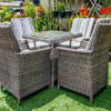 Compact grey rattan cube dining set with chairs tucked under a glass-top table on green turf.