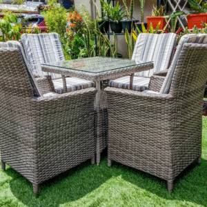 Compact grey rattan cube dining set with chairs tucked under a glass-top table on green turf.