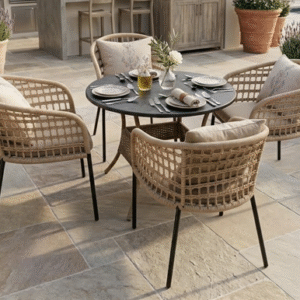 A 4-seater artisan rope weave dining set with a round charcoal table and beige cushions on a luxury stone patio surrounded by Mediterranean plants.
