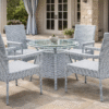 A 4-seater light grey and white rattan dining set with a round glass-top pedestal table on a stone-tiled luxury patio.